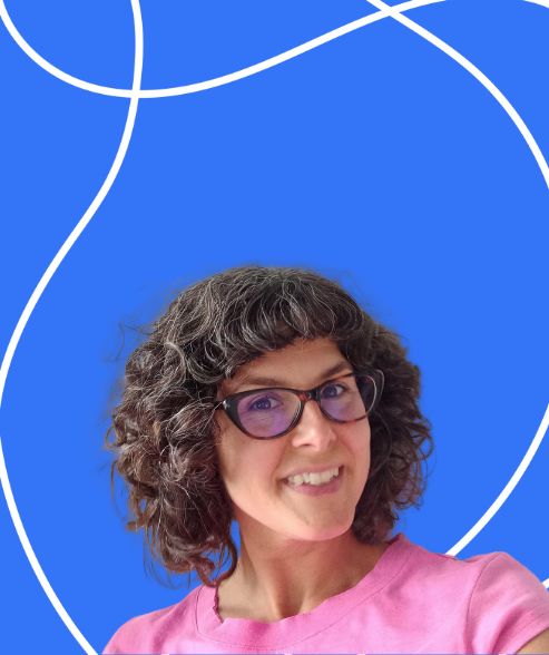 A photograph of smiling, white woman with brown curly hair, wearing dark-framed glasses and a pink/green top in front of a background of brightly coloured shapes.