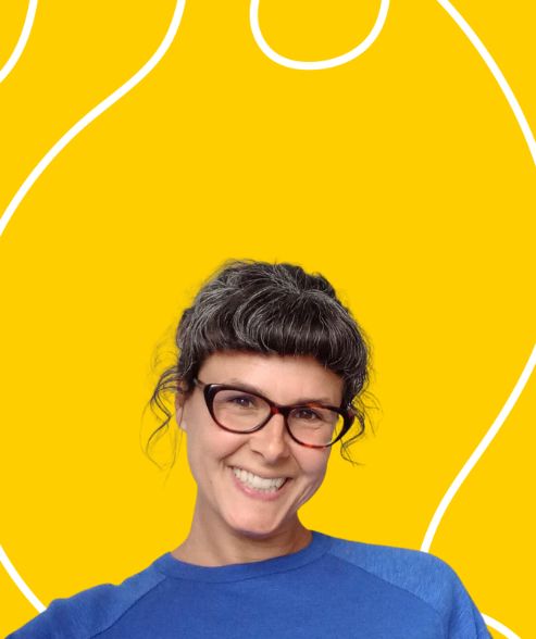 A photograph of smiling white woman with brown curly hair, wearing dark-framed glasses and a blue/green top in front of a yellow/blue background with white swirly lines around the edges of the image.