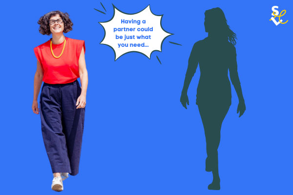 A photo of me (a brown curly-haired white woman wearing glasses, a red t.shirt, yellow necklace and navy blue trousers walking alongside the silhouette of a woman.